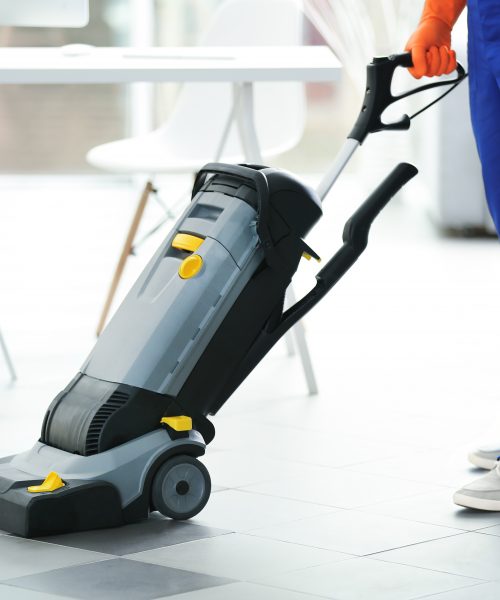 Young janitor with washing machine cleaning floor in office