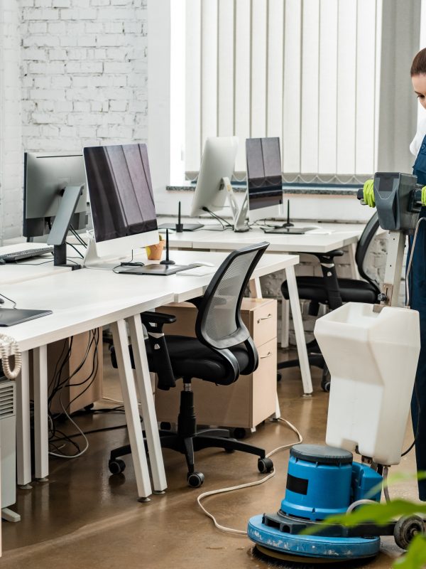 young cleaner washing floor in open space office with cleaning machine
