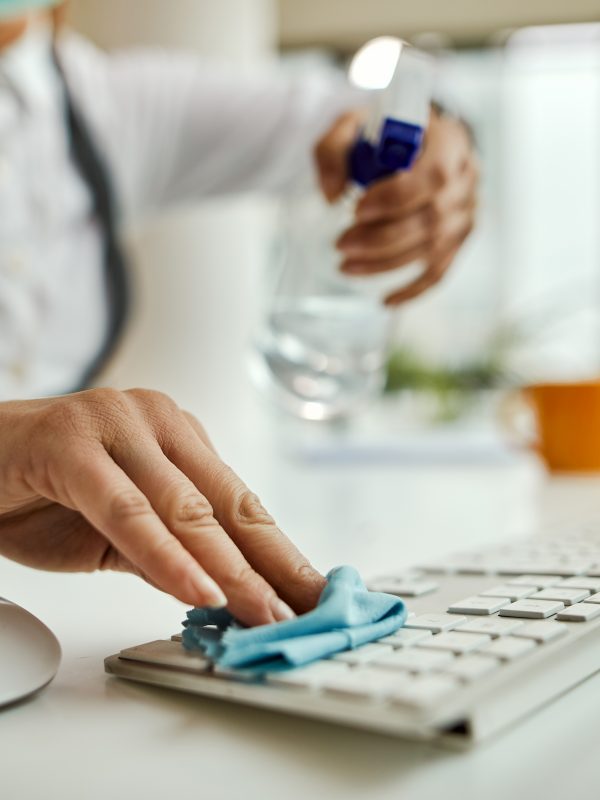 Close-up of businesswoman disinfecting computer keyboard in the office.