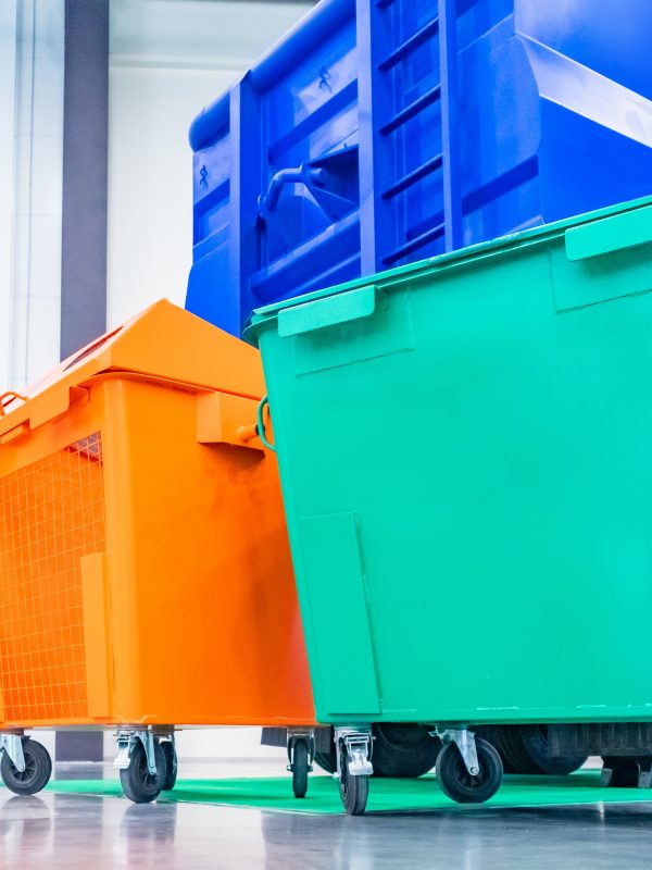 Garbage containers on wheels. Multi-colored containers next to a garbage machine. Separate waste containers. Garbage collection for subsequent disposal. Concept - care for the environment.