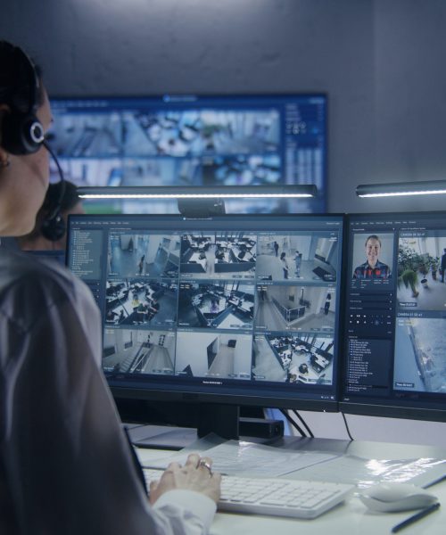Female security officer watches security cameras with AI facial recognition with male colleagues. Monitoring center workers. Computer monitors and big digital screens with CCTV cameras video footage.